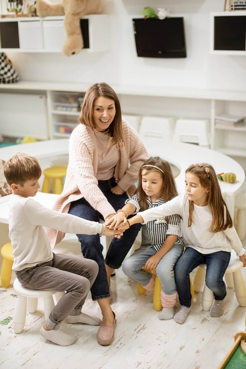 Kinder legen gemeinsam mit ihrer Erzieherin die Hände übereinander.